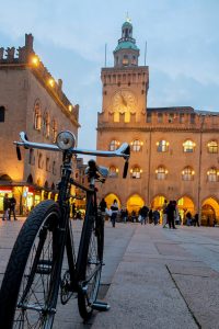 Foto di piazza Maggiore, Bologna, Italia. In primo piano una bicicletta e sullo sfondo piazza Maggiore illuminata